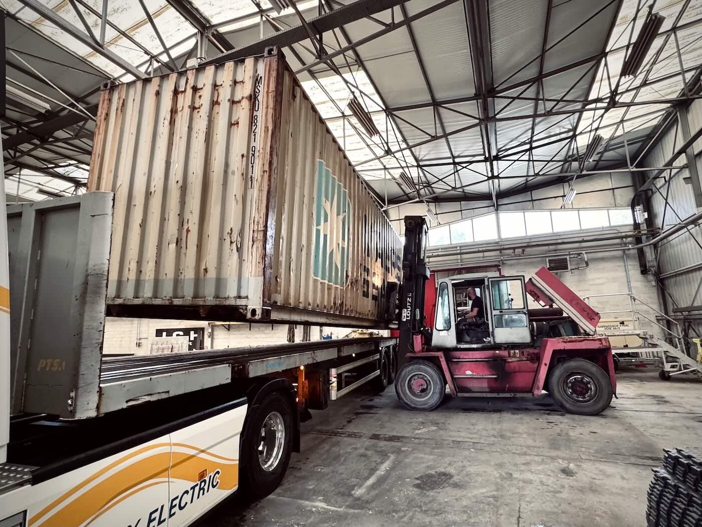 Container maritime souleve par un chariot elevateur au-dessus de la remorque qui vient de le livrer, dans la halle de transformation de JDK Concept au Havre